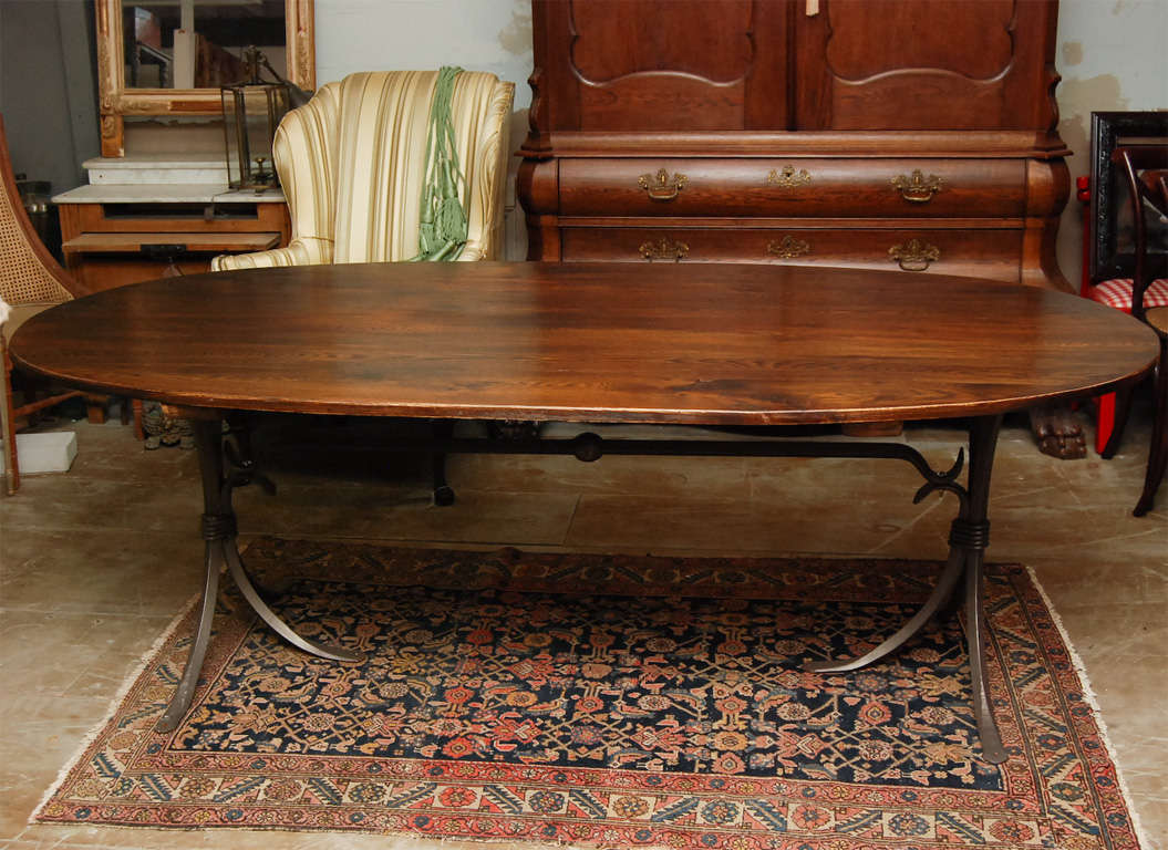 Distressed oval oak top dining table on metal base. Elegant and rustic at the same time, the wrought iron base has two three leg pedestals connected by a iron bar stretcher. Iron shows rust but can be removed and coated to protect from further