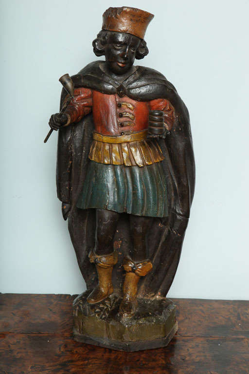 Unusual 18th Century Dutch or Flemish carved and polychromed wood tobacco figure, the cloaked figure wearing a tunic, kilt and ribboned boots, one hand holding a pipe, the other a roll of tobacco, standing on rockwork base, the whole in original