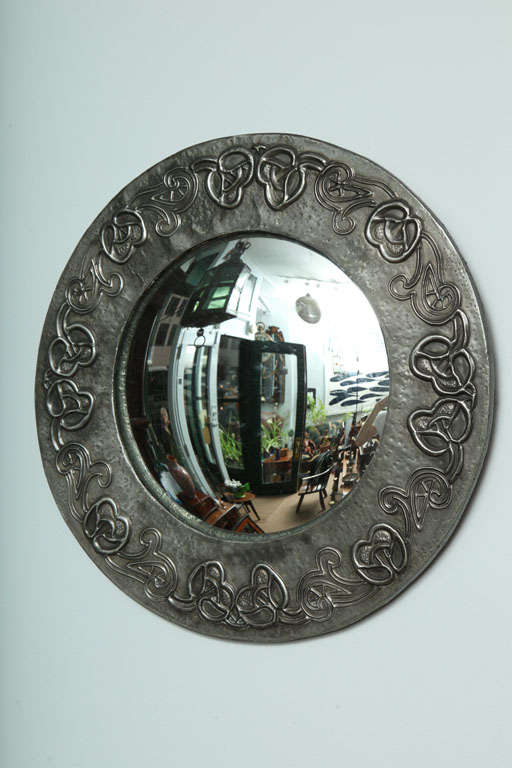 An English Arts & Crafts hand-hammered pewter round mirror having intricate woven love knot decoration in a stylized celtic manner and convex silvered glass.