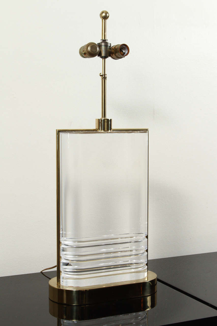 Gorgeous pair of Lucite and brass table lamps in the manner of Karl Springer.

The thick slabs of Lucite sit upon polished brass bases. The Lucite lamp bodies are clear and clean and have brass bands on each side to conceal the electrical wire.
