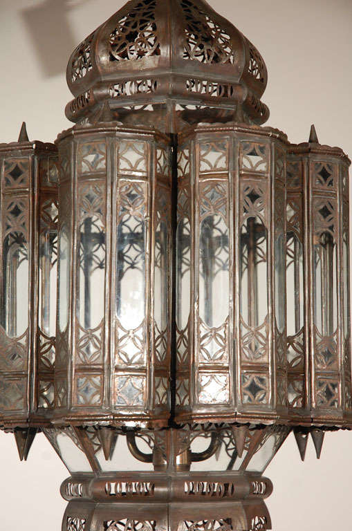 Large Moroccan lantern with clear glass multifaceted and intricate filigree work on metal, bronze patina rust finish.

Wired with 3 lights, 3 feet chains and ceiling canopy.
A pair is available. Price is for 1 light fixture.

Mosaik provides