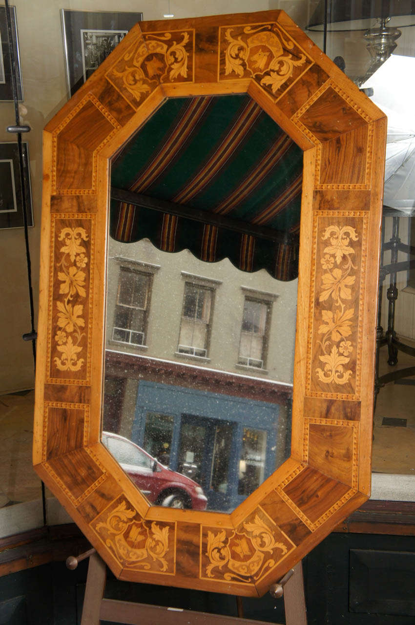 This lovely mirror inlaid in marquetry of walnut, rose wood  and fruit wood shows the cabinet makers deft hand. The images are of flowers ,leaves and heraldic images all within lozenges surrounded by contrasting checked borders. The shape an