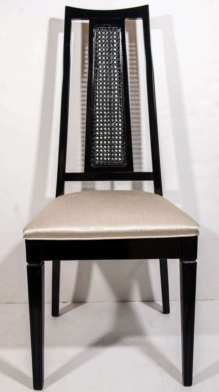 Set of four mid-century modern dining chairs with elegant high back design. The chairs have an trapezoid back with cut-out details and cane back center.  Ebonized walnut wood finish, and upholstered in champagne colored woven silk, with self welt