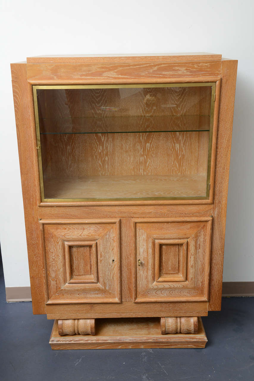 Art Deco, in cerused oak, the upper part is opening by a bronze framed glass door. The upper inside part with  glass shelf is lighted from the top.
Locked with an adorable small bronze key.
One glass shelf in the middle of the vitrine.
The bottom
