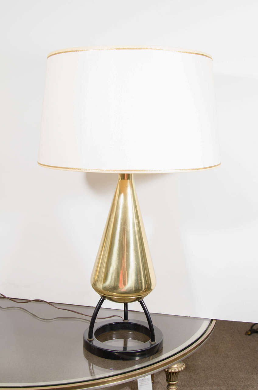 A lovely pair of midcentury tripod table lamp with brass vase shape body mounted on three legs and a circular black enamel base. Vintage drum shades with gold braid top and bottom trim.