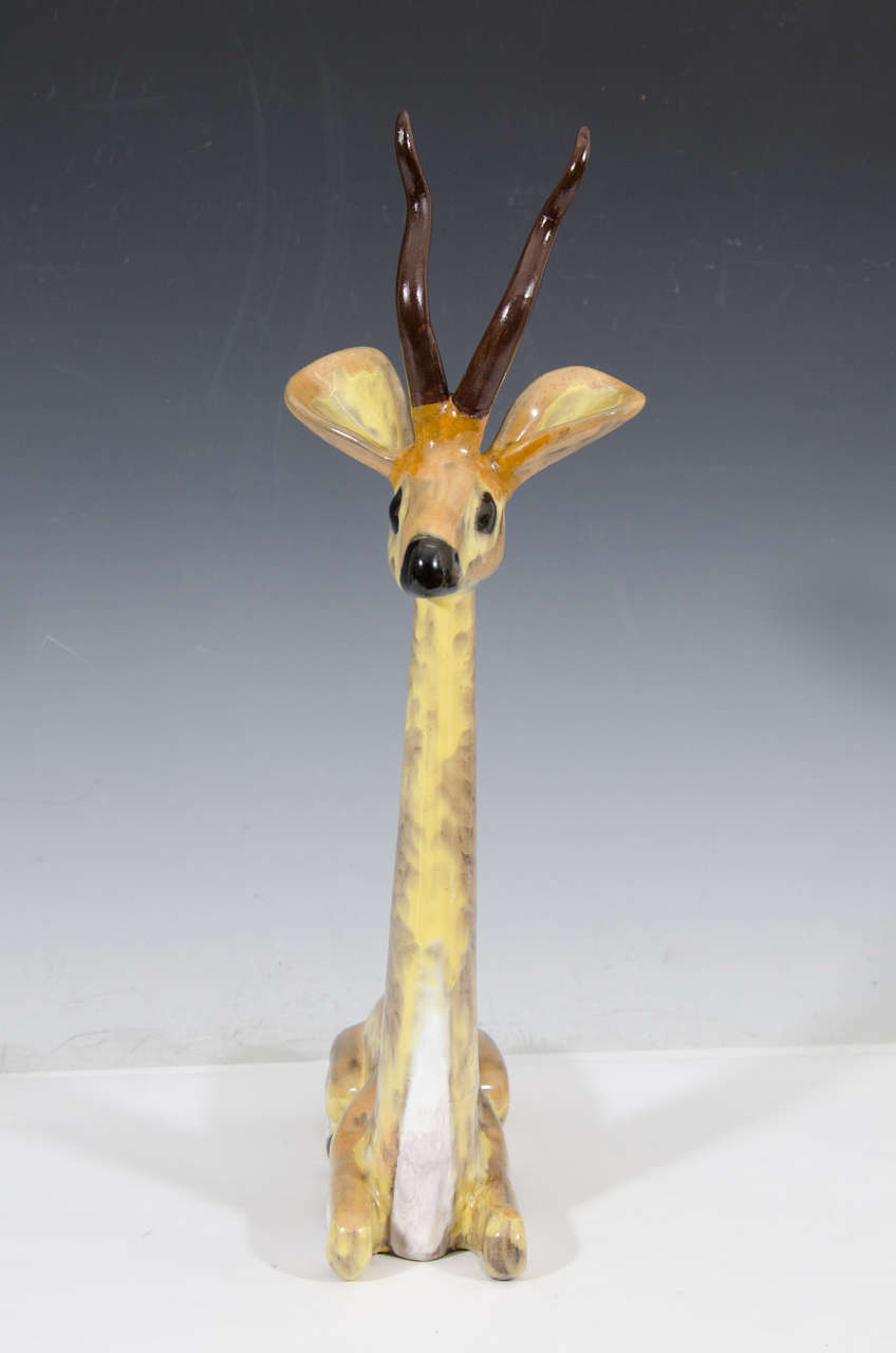 A vintage ceramic sculpture of a seated antelope in golden yellow, white, and shades of brown.  Good vintage condition with age appropriate wear.  Some hairline cracks due to age.