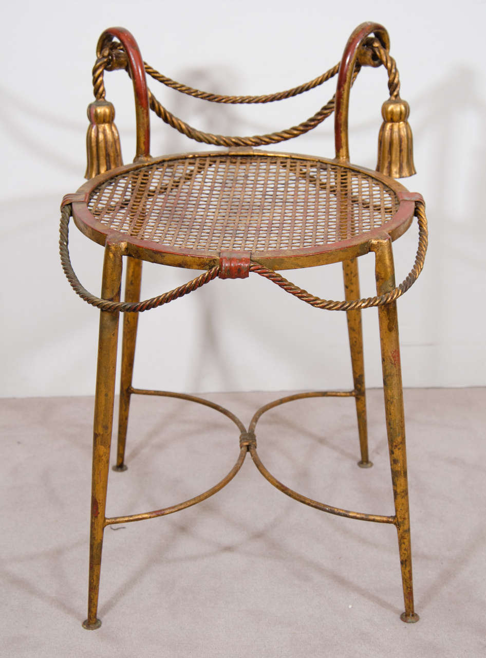 A vintage Italian gilt metal stool with rope and tassel adornment and painted in a red wash finish. Good vintage condition with age appropriate wear.