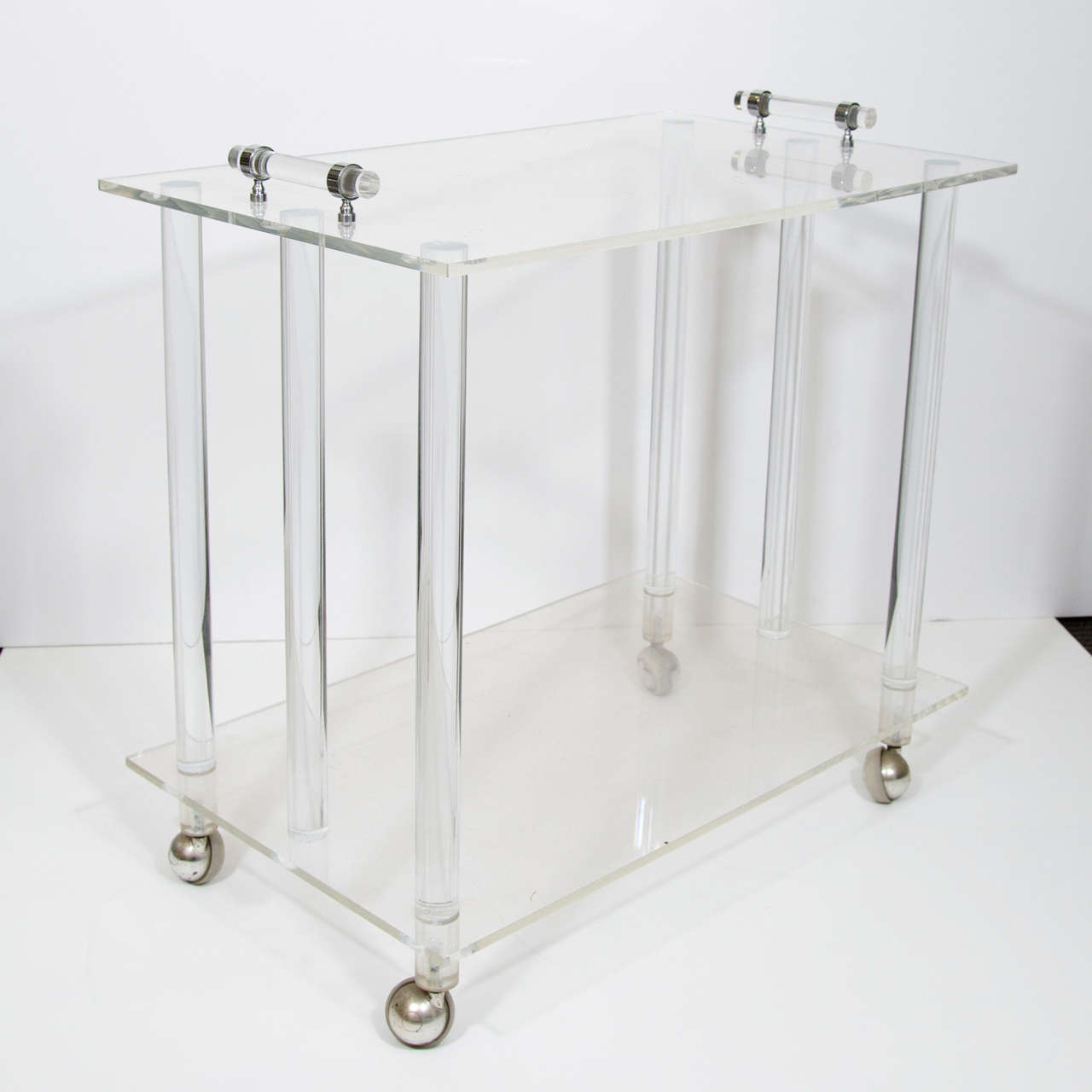 A vintage, highly modernistic two-tier service and bar cart, produced circa 1970's, with push handles, the two surfaces supported by six cylindrical columns, entirely in lucite, on casters. This cart can elegantly display your barware, spirits, and