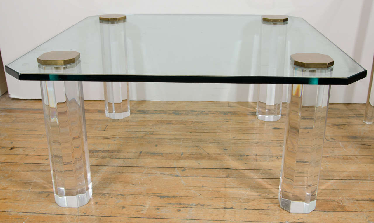 A vintage coffee or cocktail table with glass top on thick Lucite octagonal column legs with brass caps, produced circa 1970s. Good vintage condition with age appropriate wear and patina. Some minor scratches to the glass.