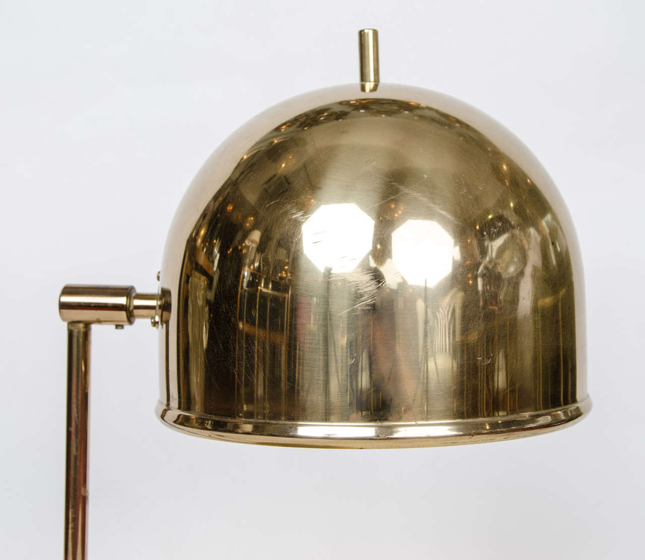 Adjustable tilting head domed brass table lamp with simple brass arm and circular stand.
