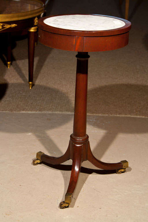 Regency style mahogany side table, the circular top with marble inset supported by a single pedestal, raised on tripod splayed legs ending in brass casters.