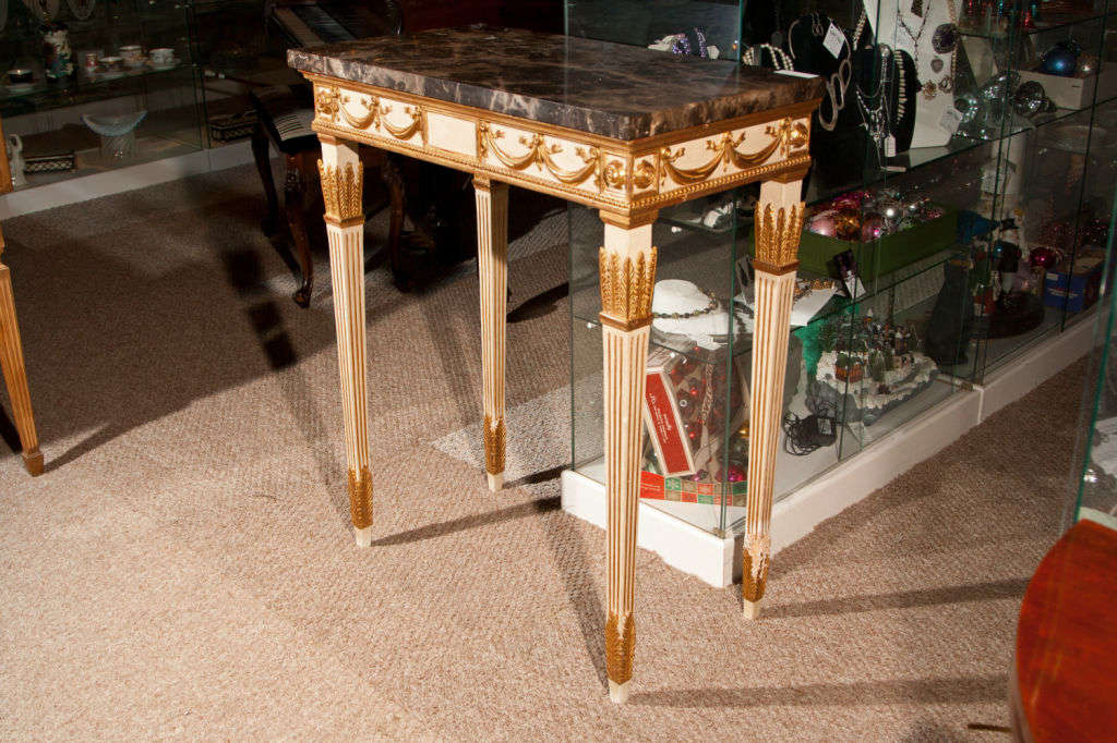 Pair of fine English Georgian style console tables, each creme-peinte and parcel-gilt, the rectangular dark grey marble above a narrow frieze decorated with garlands, pateras and beading, raised on four fluted tapering legs. Provenance: Home of
