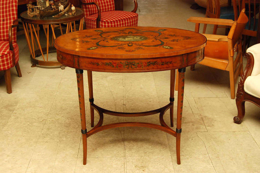 Oval center table in satinwood, Edwardian period, painted and decorated in the manner of Angelica Kaufmann, Sheraton style.