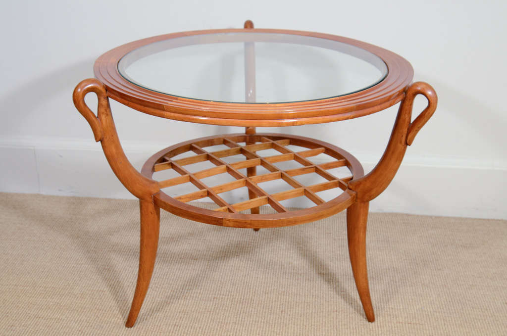 The circular fluted wooden top supporting a clear circular glass top, with wooden trellis shelf below, raised on three tapering serpentine wooden legs.