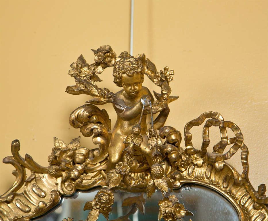 A lovely French Art Nouveau style giltwood mirror, Late 19th Early 20 Century. The oval looking glass with elegantly carved frame, the top decorated with a cherub. Minor losses.