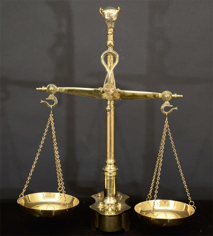 Bronze and Brass Balance Scale.  A Detailed Bronze Bull's Head Supports A Brass Balance Rod Ending With Poised Dolphins Supporting Three Chain And Weighing Pans.  The Base Contains Ten Graduated Weights.
