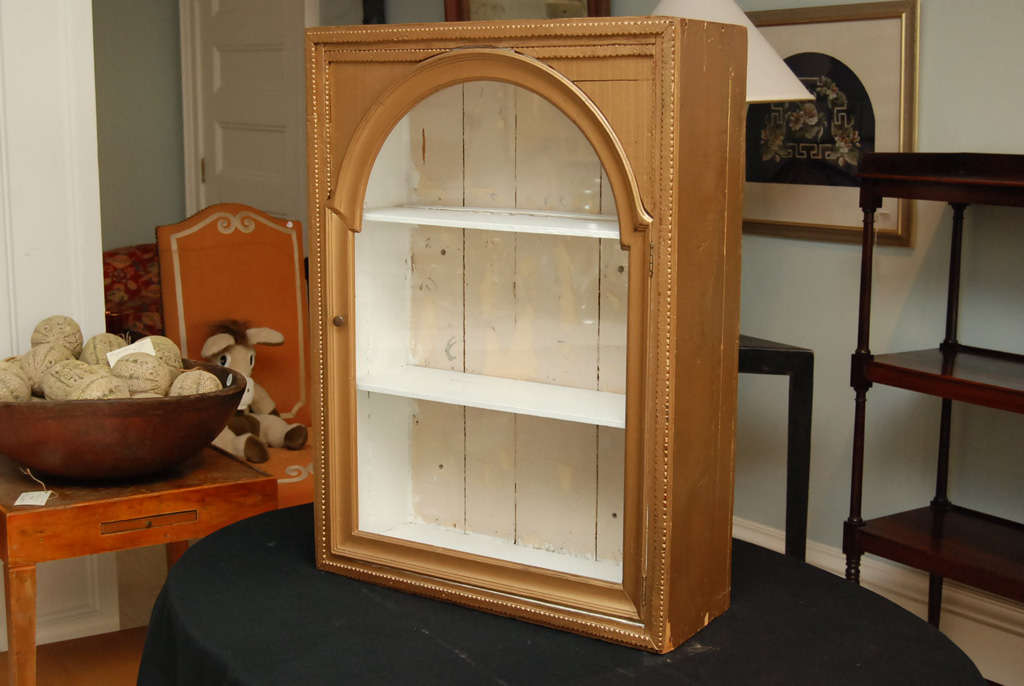 Gold Tramp Art hanging cabinet with white painted interior and two shelves. Glass door.