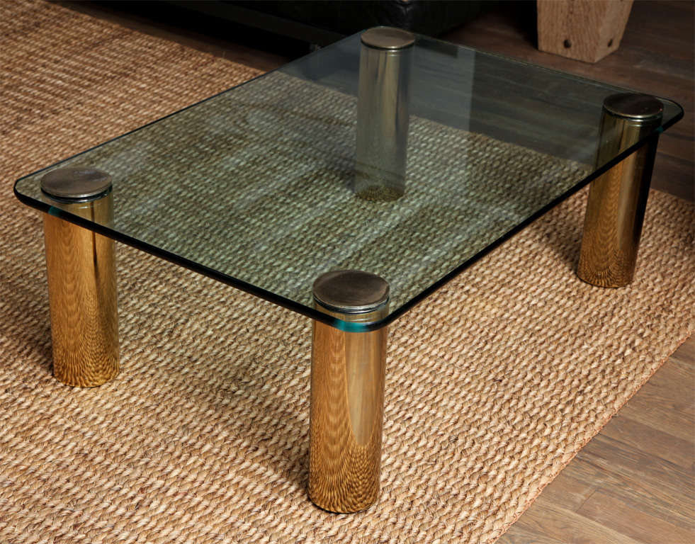 A coffe table by Karl Springer with cylindrical brass legs mounted in to the glass top.