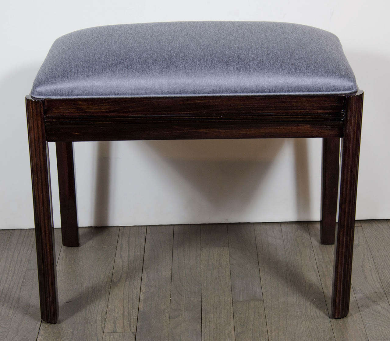 This bench/ stool features a fluted leg detailing and is made of ebonized walnut and newly upholstered in a silver /blue sharkskin upholstery. Great as a bench / stool for a vanity or a hallway. This piece has been mint restored.