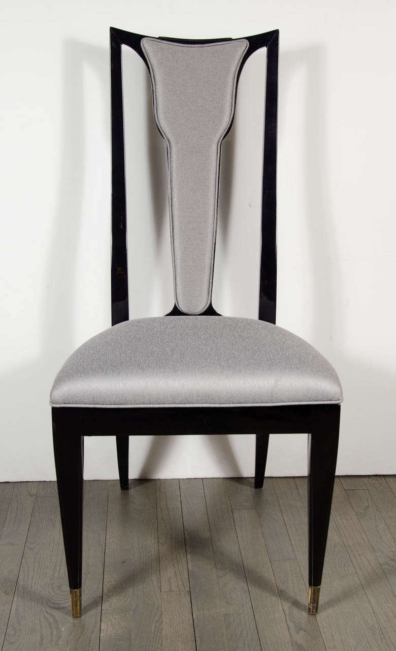 This sophisticated set of six Mid-Century Modernist ebonized walnut chairs features brass sabots on the front legs, cabriolet hind legs, and a skyscraper style back with a trophy form in the center. Two of the chairs include arm rests, making them
