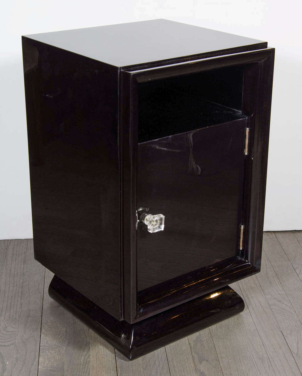 This elegant pair of shadow box nightstands/ end tables were realized in the United States, circa 1950. Realized in beautiful ebonized walnut, they feature a plinth base,  a cut out shelf space above a cabinet concealed by a door fitted with a