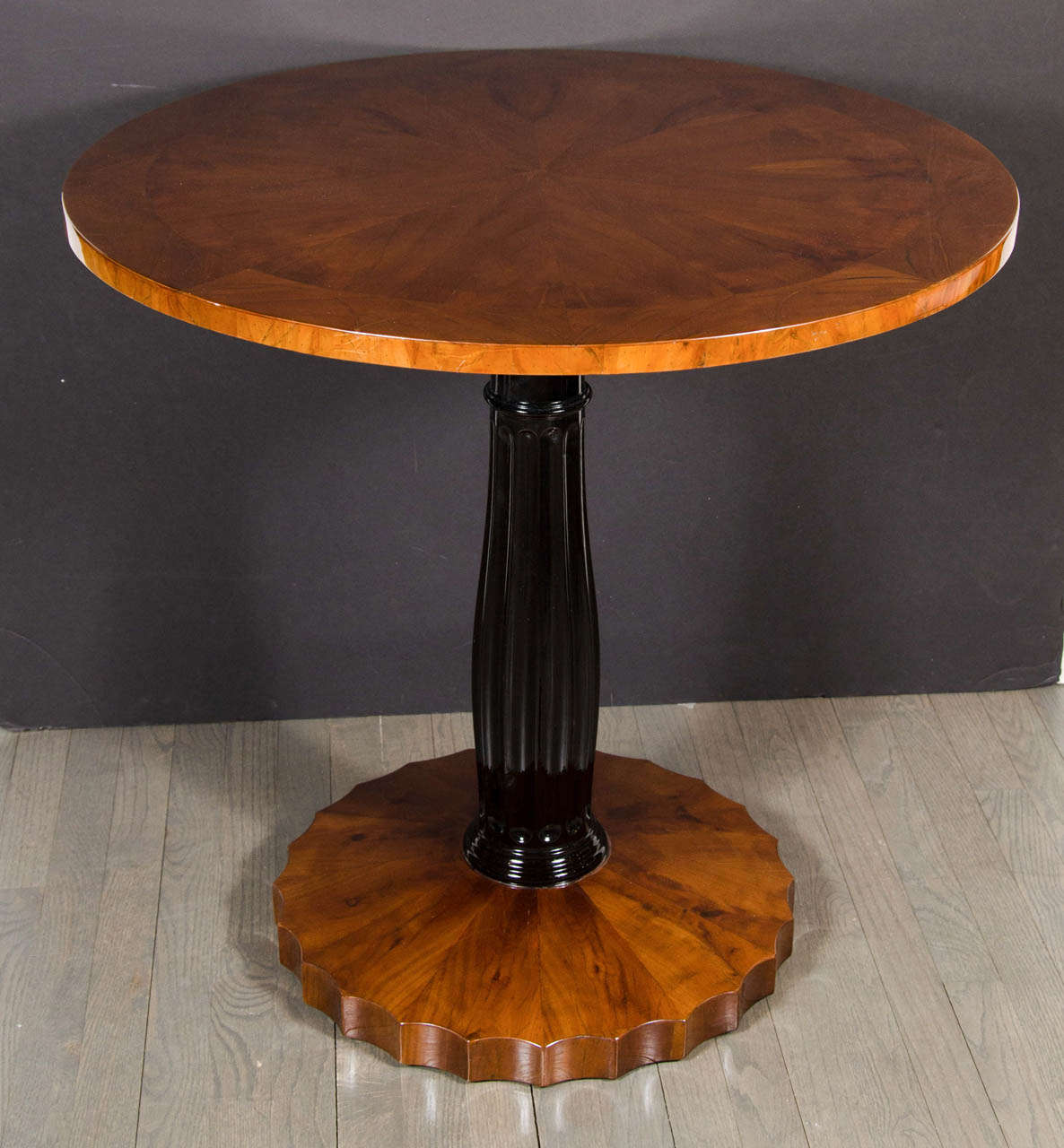 This stunning table features a top with an inlayed starburst design of exotic walnut supported by a fluted ebonized pedestal with  an inlayed book-matched walnut scalloped base.This table has been mint restored