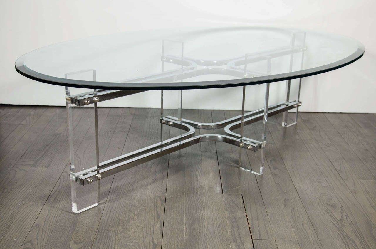This chic Mid-Century Modernist cocktail table consists of a streamlined chrome frame with Lucite supports. The table top is hand beveled oval clear glass.