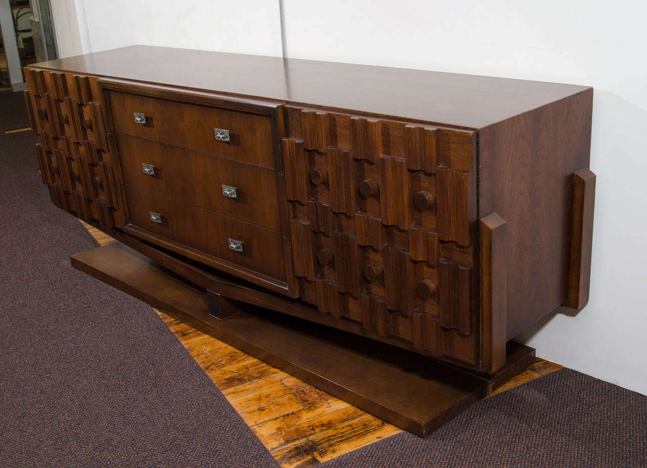 A vintage hand carved wooden dresser on a pedestal base with mosaic block panel doors and molten lava relief hardware in the style of Paul Evans. Comes with matching mirror. Good vintage condition with age appropriate wear.  Some wear to the wood