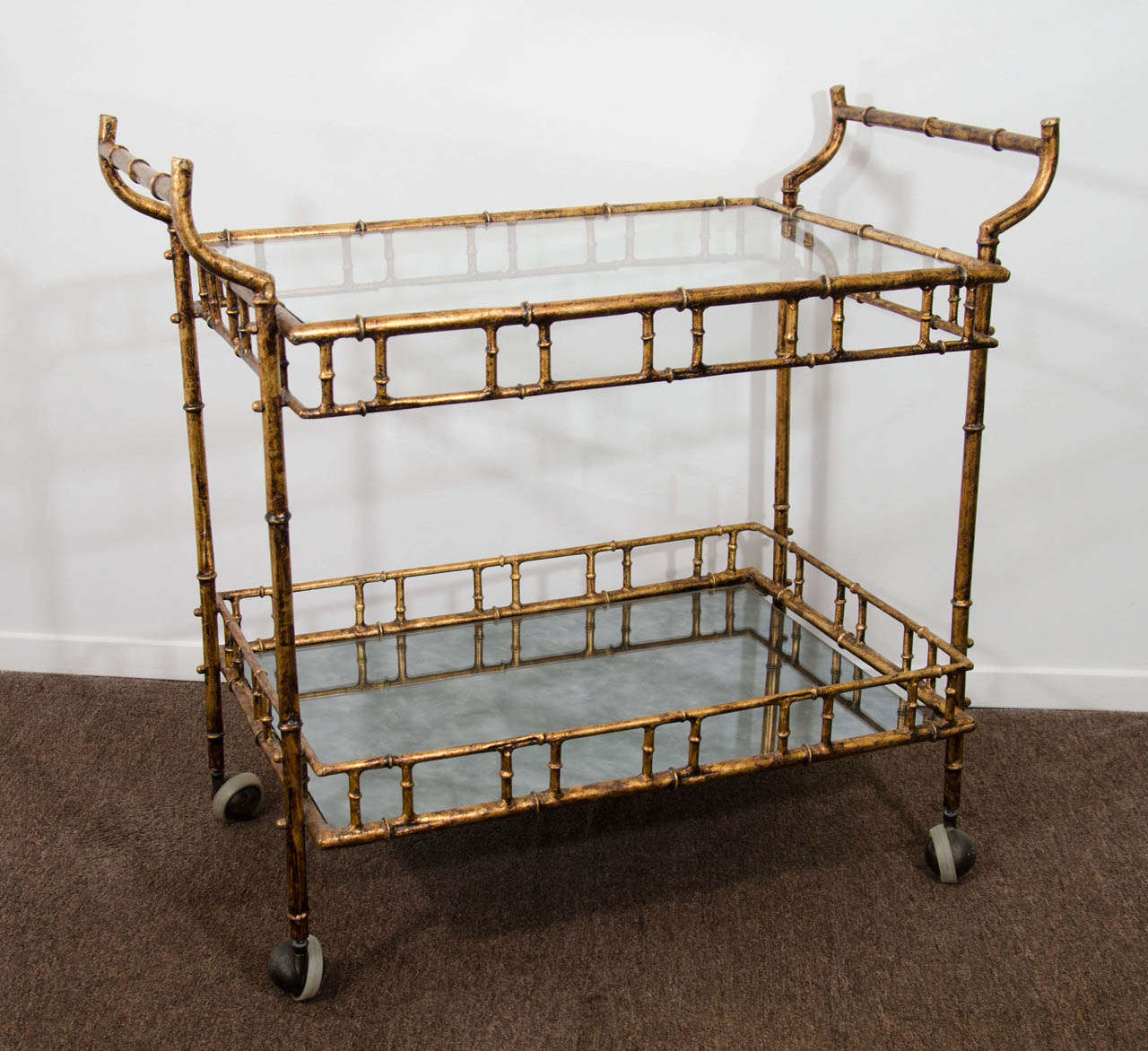 A vintage Faux Bamboo gilded metal two-tier and glass double handled bar cart in the style of Maison Bagues.

Good vintage condition with age appropriate wear.  Some scratches and wear to gilded metal and wheels.