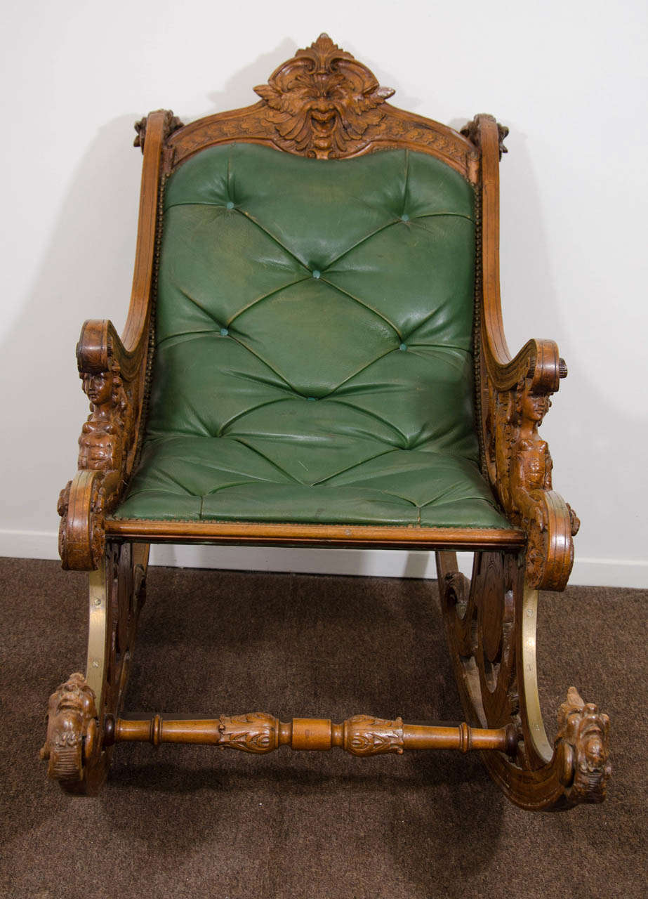 A 19th century carved walnut Italian rocking chair with griffins and rams heads.  The seat is upholstered with green button tufted leather and has brass nail head detailing.

Good condition with age appropriate wear.  There are some scratches to