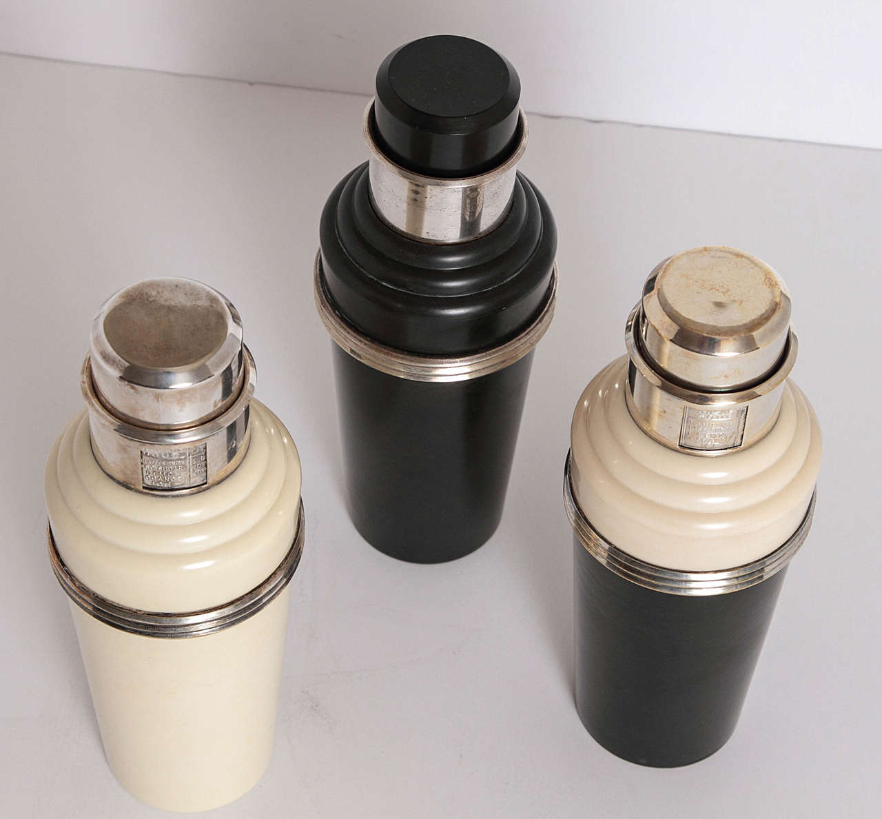 Classic 1930s English shakers.

(1) Original white phenolic body, with silver plate trim ring, cap, spout, strainer and revolving neck recipe dial. Complete and signed.

(2) Original black phenolic body and cap, with silver plate 