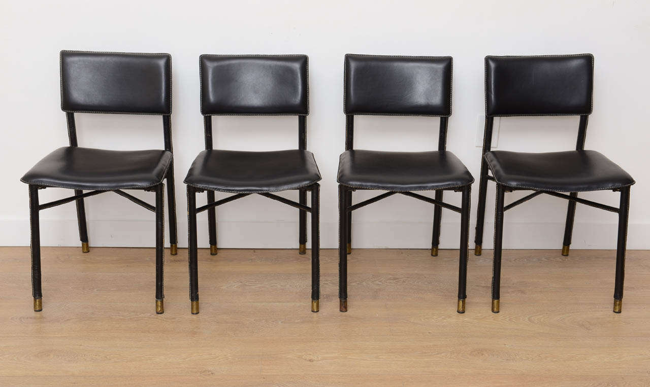 Four hand stitched black leather chairs with brass sabots by Jacques Adnet.