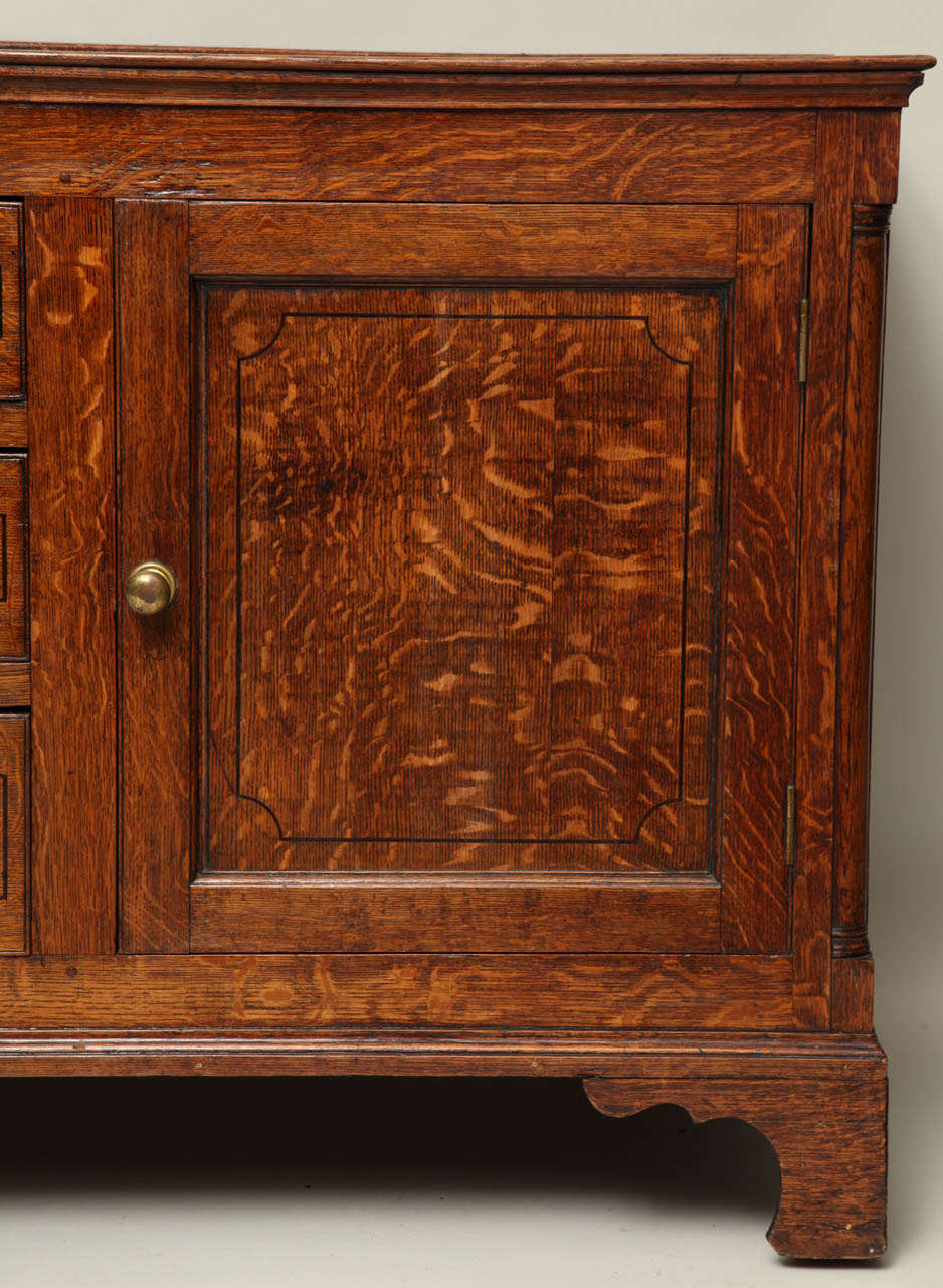 Very fine George III English low dresser of cabinet from in vividly grained quarter sawn oak, the top with original plate rail over pair of paneled doors flanking a row of three drawers, all with ebony string inlay, the case with quarter columns and