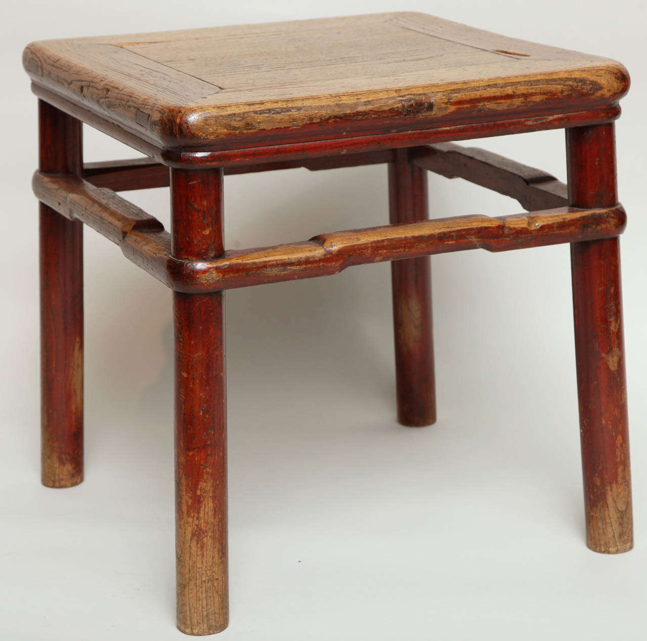 An 18th century Chinese elm square table, the single board top with mitered panel construction, over pole turned legs joined by stepped stretchers, retaining crimson lacquer surface in places and worn to a rich patina, the whole with good color.