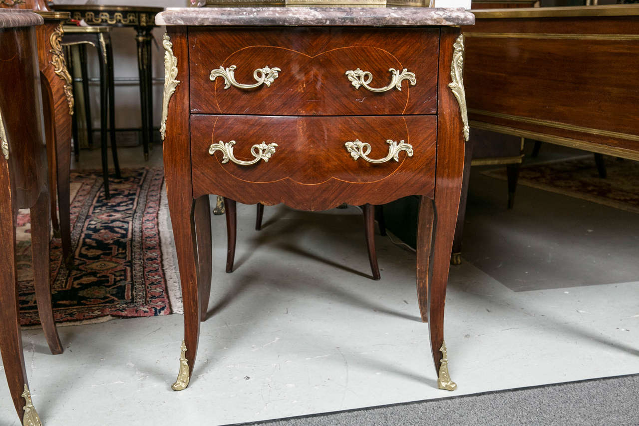 Pair of bronze-mounted Louis XV style end tables. A fine French pair of marble top commodes in the Louis XV fashion. The bronze sabot feet supporting a case of two drawers with bronze mounts and pulls. Each shell of bombe form with a fine grayish