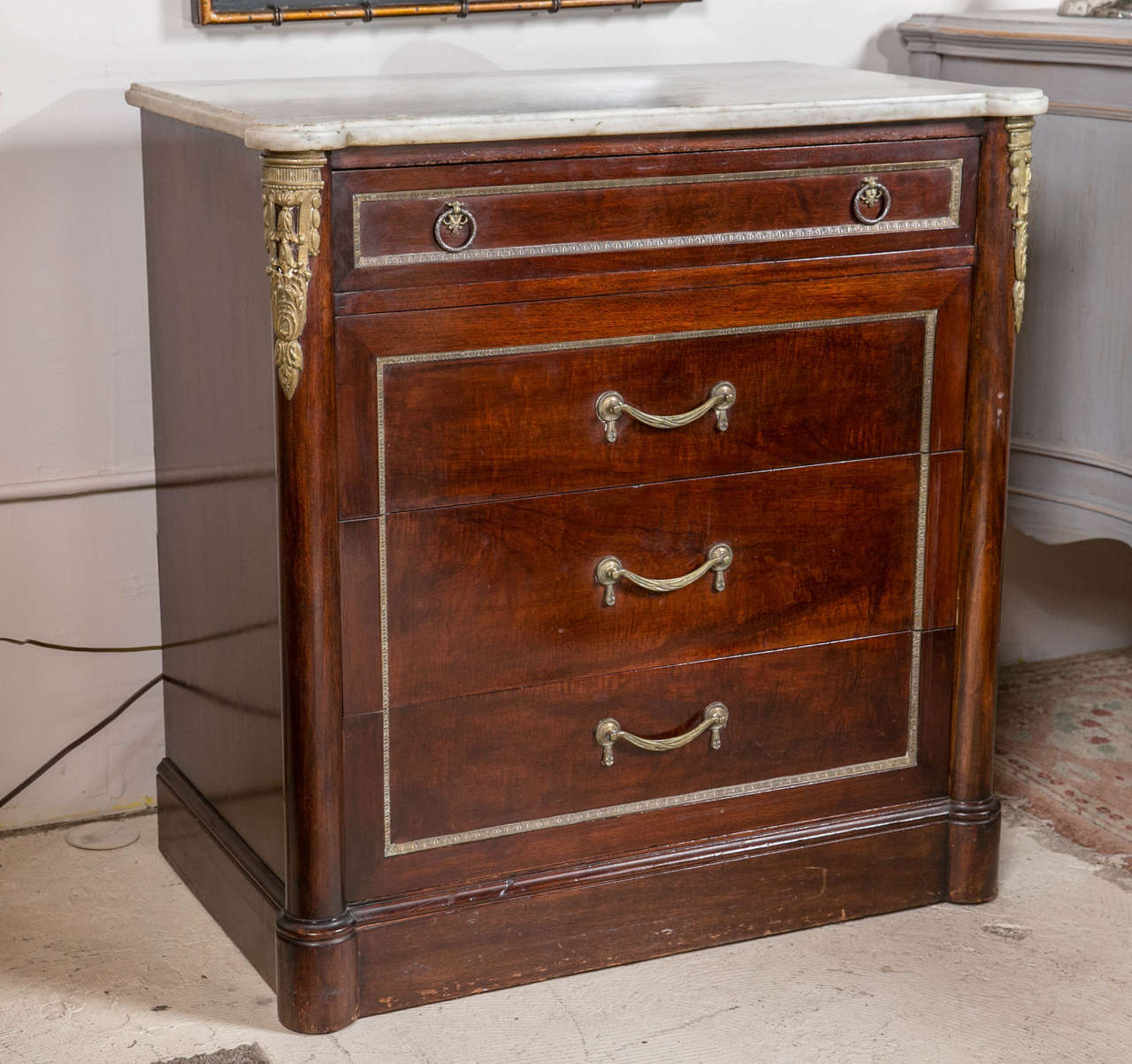 Pair of mahogany marble-top mahogany commodes. A fine pair of solid mahogany marble top commodes. Each having a central bronze framed smaller drawer over three large bronze framed drawers. The corners with finely cast bronze mounts. Fine custom