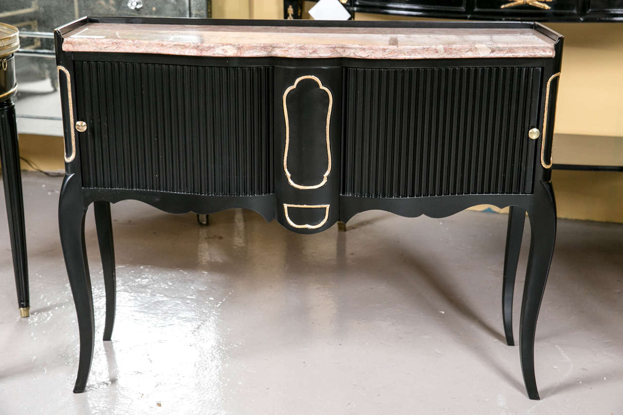 An ebonized marble-top console or serving table with tambour doors. The Louis XV style console has gilt gold hi lights on the ebony polished cabinet case with a center panel flanked by tambour doors with brass pulls. The whole supporting a fine pink
