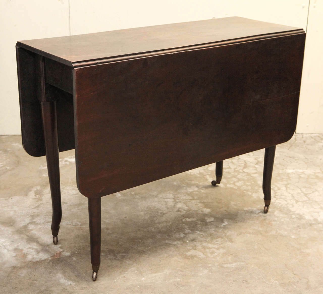 Late 18th century plum pudding mahogany drop-leaf dining, gaming, or side table from England. Legs with bronze castors are able to extend the table.