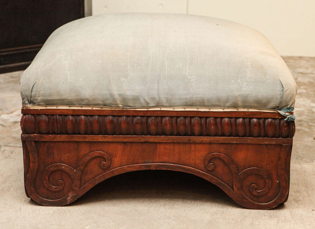 An Italian 1830s ottoman or footstool in hand-carved fruitwood with muslin upholstery. Detailed carving around the base of the stool.