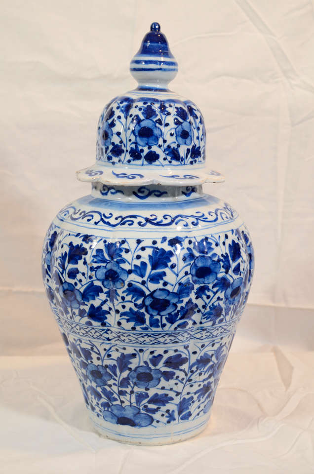 A pair of brightly painted Blue and White Dutch Delft vases with an allover design of flowers and leaves. The covers have attractive scalloped edges, and traditional striped finials. 