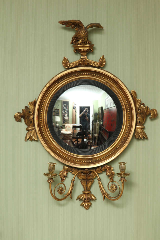 Very fine Regency carved and giltwood convex mirror having an eagle and leaf carved surmount above a moulded frame having a bead carved interior with a fluted ebonized inner frame and the original mirror plate. The sides having applied acanthus leaf