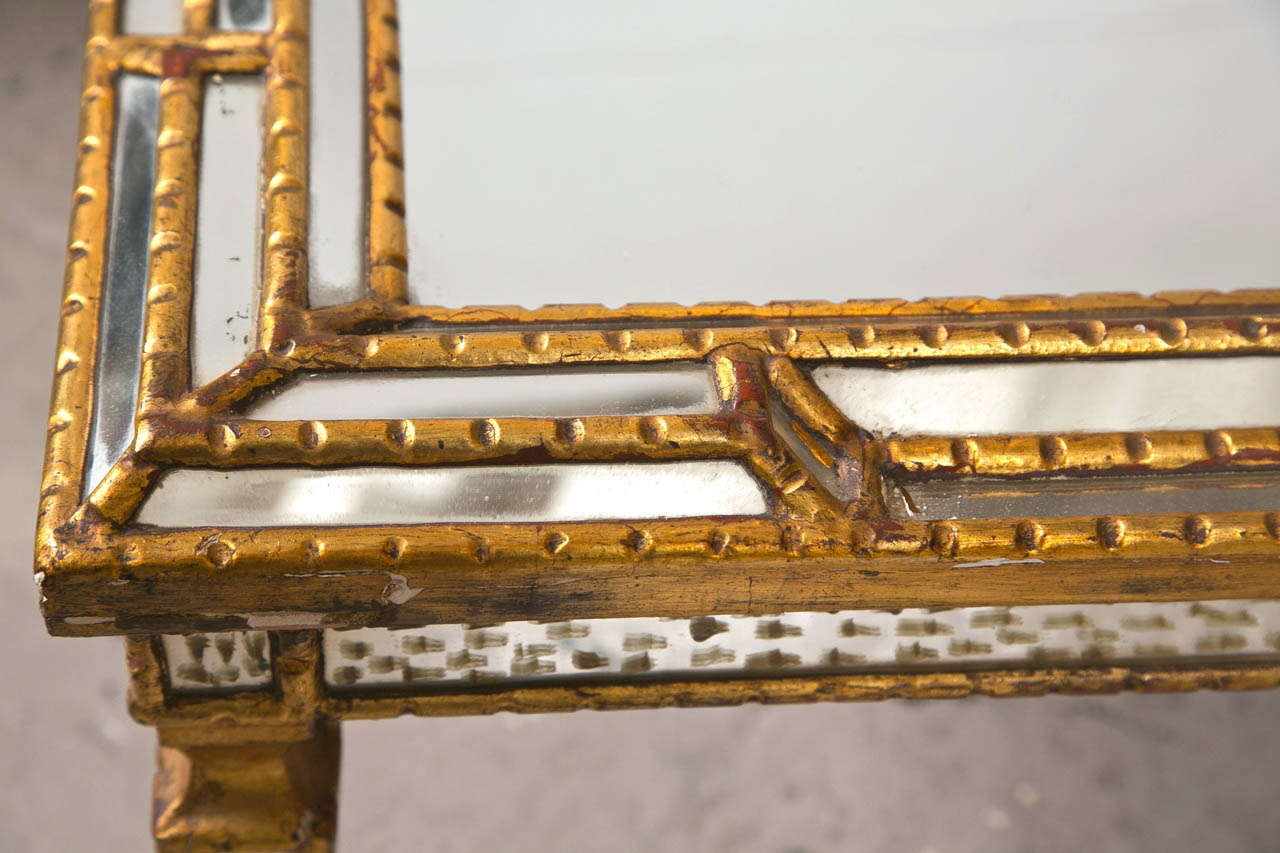 An Art Deco style coffee or cocktail table, 20th century, the rectangular mirrored top with raised gilded wood frame, supported on mirror veneered squared tapering legs, ending in pegged feet.
