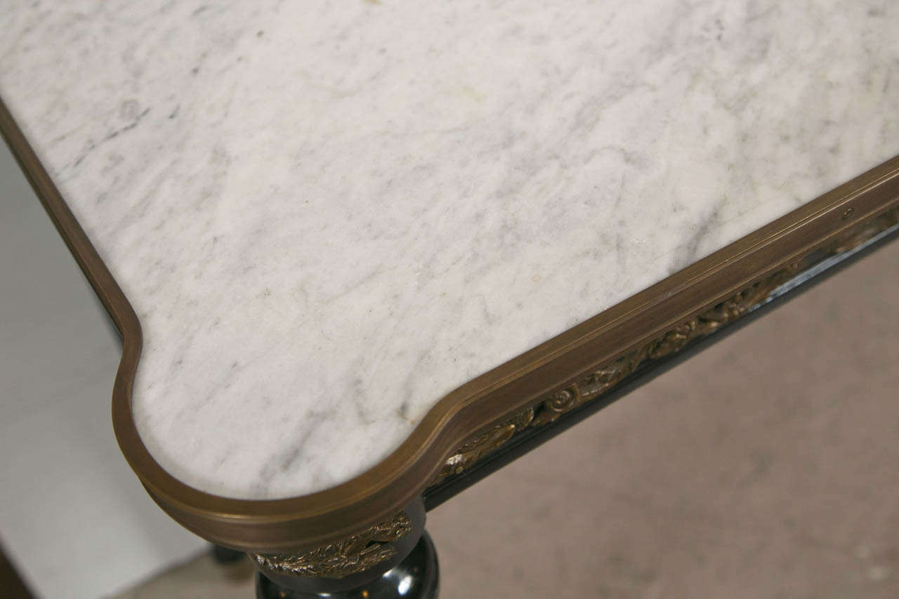 A French Directoire style console table, overall ebonized, the white marble with bronze banding over a frieze decorated with bronze mounts, raised on circular tapering legs, ending in capped feet.