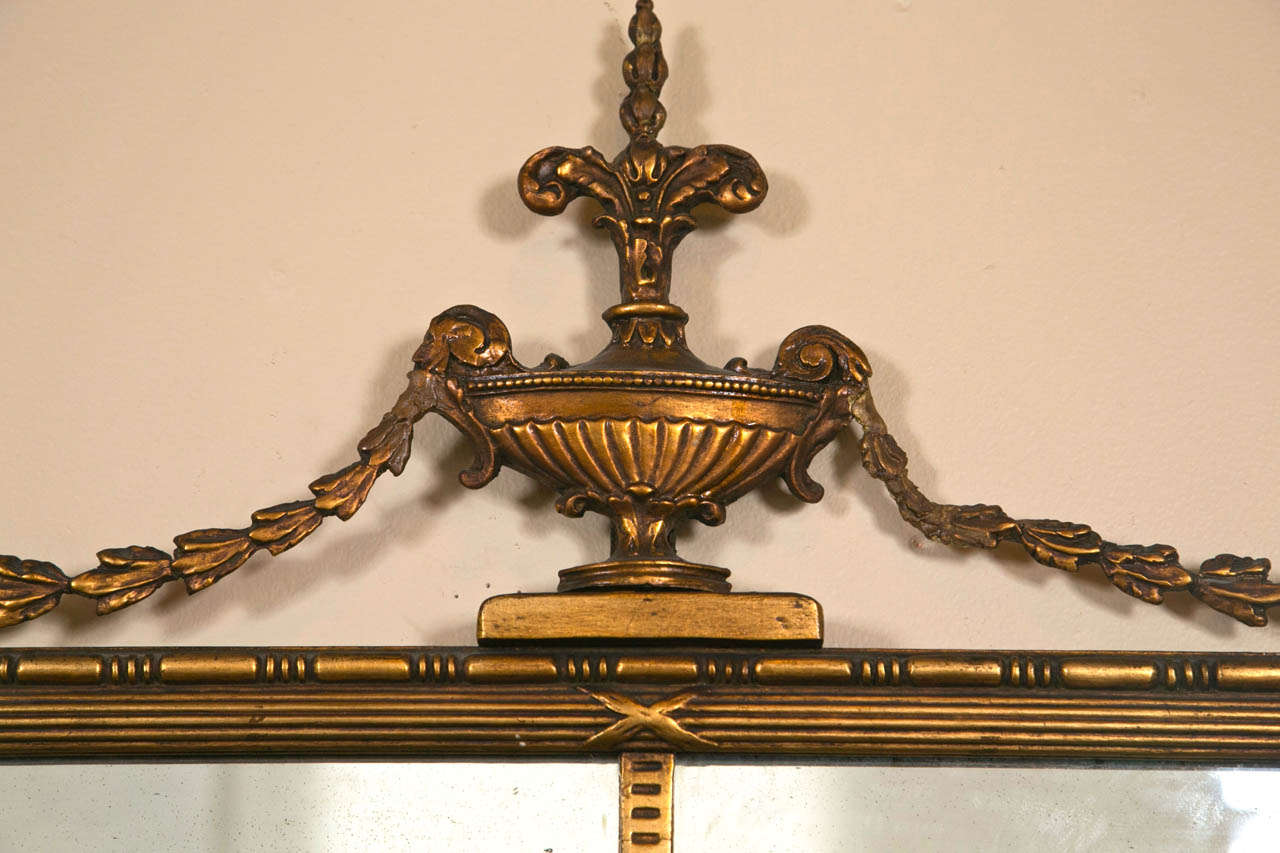 An early Adams style giltwood mirror. This Adams style mirror set to give a 19 panel appearance. The giltwood border holding a group of framed border wooden panels. The top with an urn crest flanked by a flowing leaf and vine design.