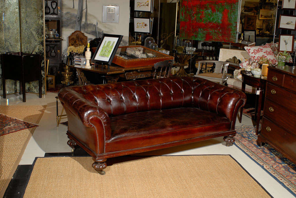 A fine quality early 19th Century English Chesterfield sofa covered in early 20th Century cognac colored leather. The tufted button back and solid bench seat are flanked by panel arms with decorative nail trim on the inserts.  All resting on a solid