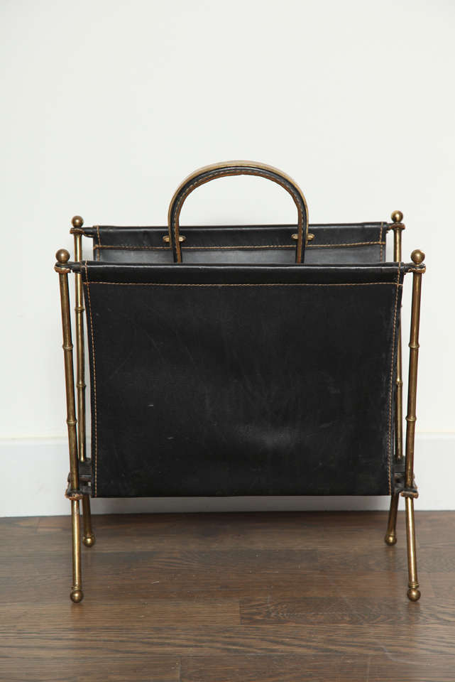 A magazine rack by Jacque Adnet in black leather with detailed brass frame and accents,  plus an excellent condition report all make this a great collectable.