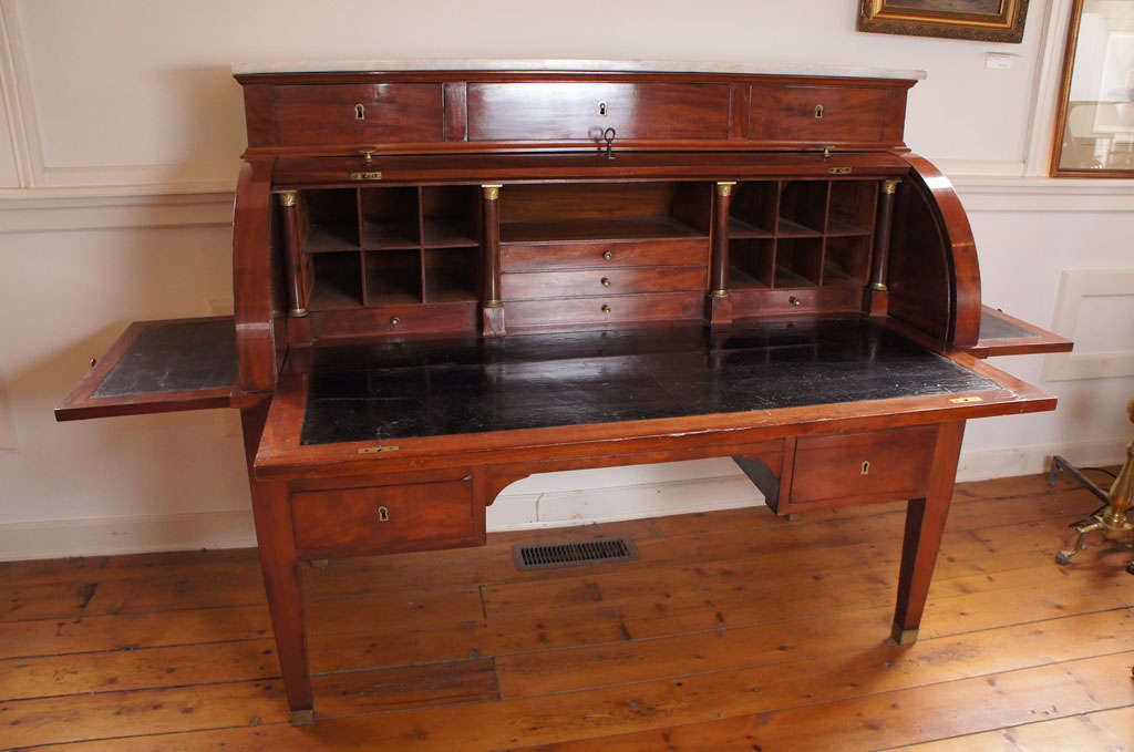 Fine French Mahogany roll top desk. White marble top over three drawers. Interior with cubby holes and drawers . Black leather writing surface and slides. Hidden drawer on the left. On tapering legs with brass cap toes and casters. Oak secondary