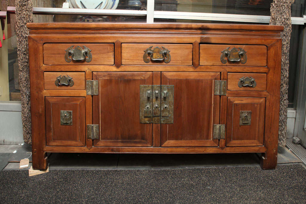 A Chinese elm sideboard with multiple drawers and two doors from the late 19th century. This Chinese sideboard was made in elmwood in an unusually narrow shape, and adorned with brass hardware. The sideboard features two center doors, surrounded by