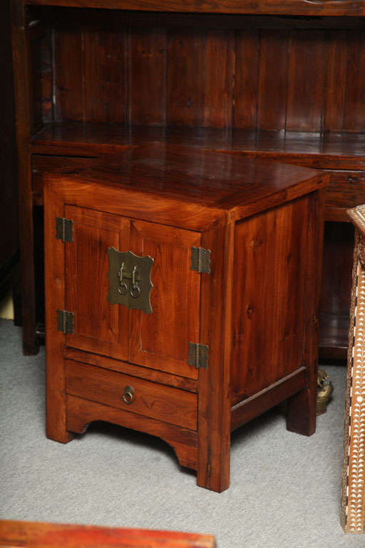A small Shanxi style elmwood bedside cabinet with two doors, single drawer and patinated brass hardware from the turn of the century. This bedside cabinet was hand made with elmwood and brass in the Shanxi style, common in parts of Northern China at