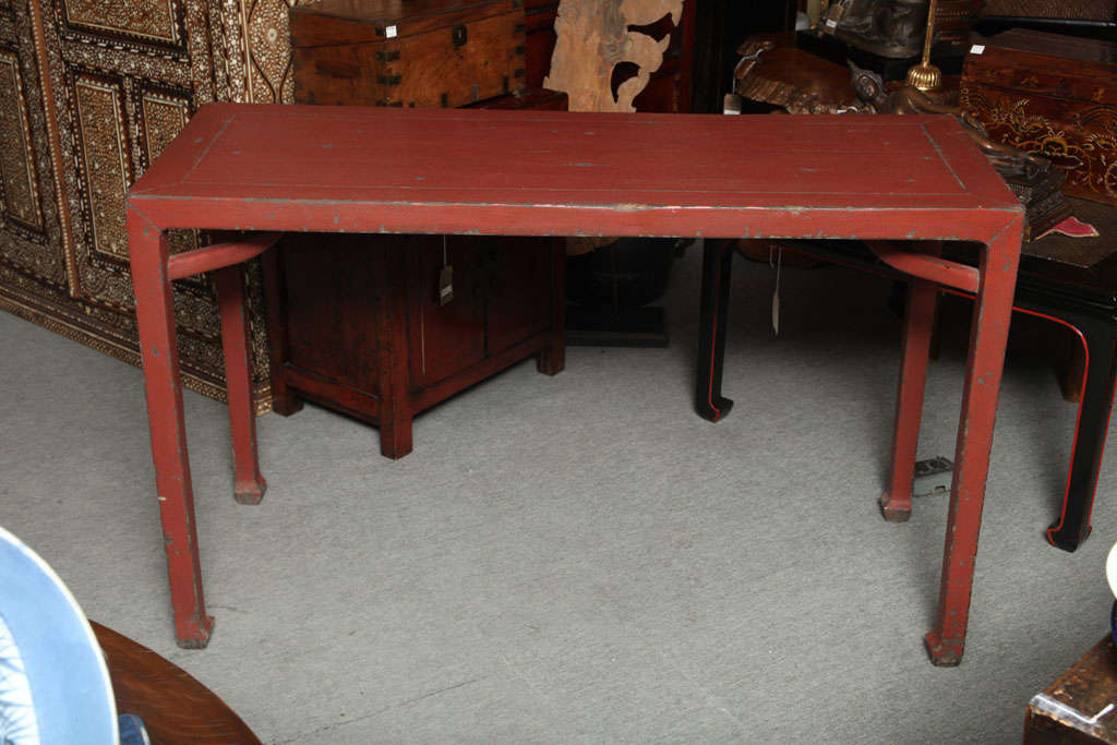 A 19th century Chinese red lacquered elmwood linen covered console table. This table adopts an unusual classic shape as the legs are finished with light scrolls and are reinforced with stretchers under the top. The table is made with red lacquered